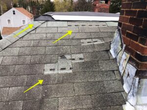 Damaged asphalt shingle roof in Lincoln, RI, showing storm damage and missing shingles near chimney flashing.