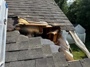 Storm-damaged roof in Coventry, RI, showing missing shingles, exposed wood, and gutter damage.
