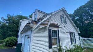 Storm damaged roof in Newport, RI with missing shingles and exposed wood. Siding is also damaged.