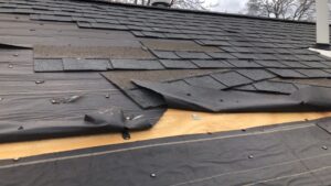 Storm-damaged asphalt shingle roof with missing shingles and exposed underlayment in Wickford, RI.