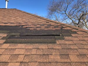 Storm damaged roof in South Kingstown, RI, with missing asphalt shingles and exposed underlayment.