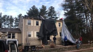West Greenwich, RI home with roof storm damage, tarp covering, and workers on roof