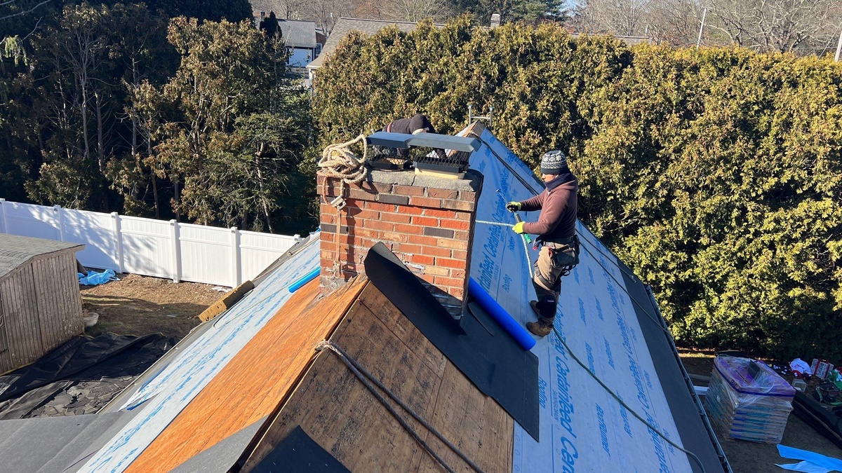 Crew installing ice and water shield at chimney Smithfield RI roof repair